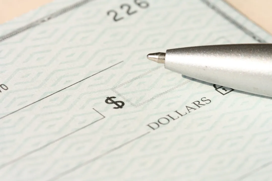 A pen rests on a check near the dollars line.