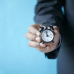 a man in a suit holding a small alarm clock
