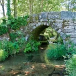 Stone bridge arches over a clear, shallow stream.